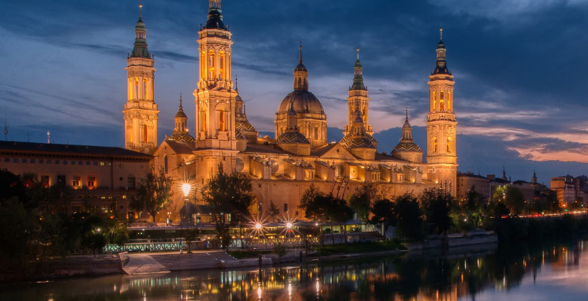 A cathedral is lit up at dusk by a river.